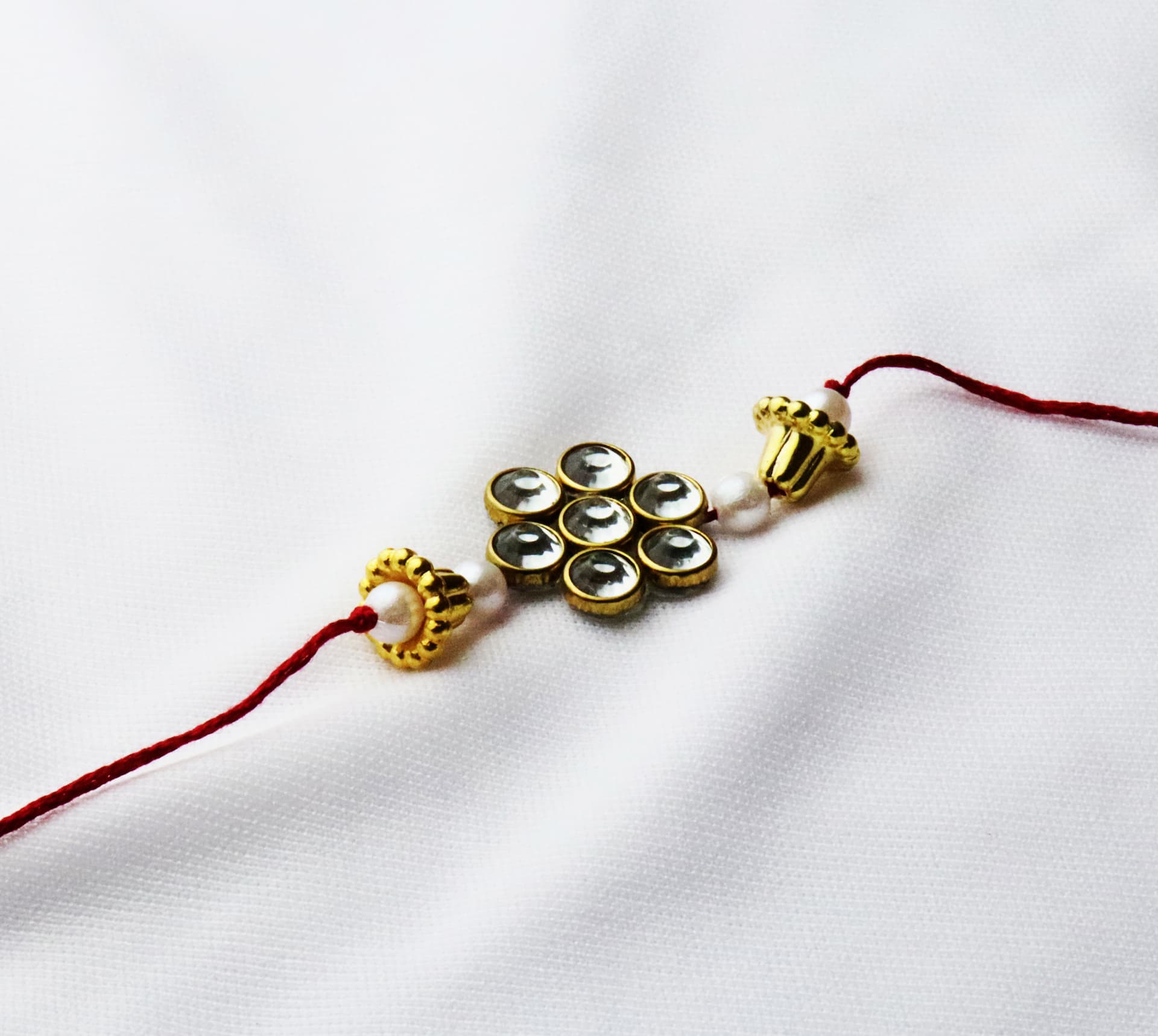 Elegant Kundan Floral Rakhi with Pearl Accents on Red Thread ( 12 Pcs )